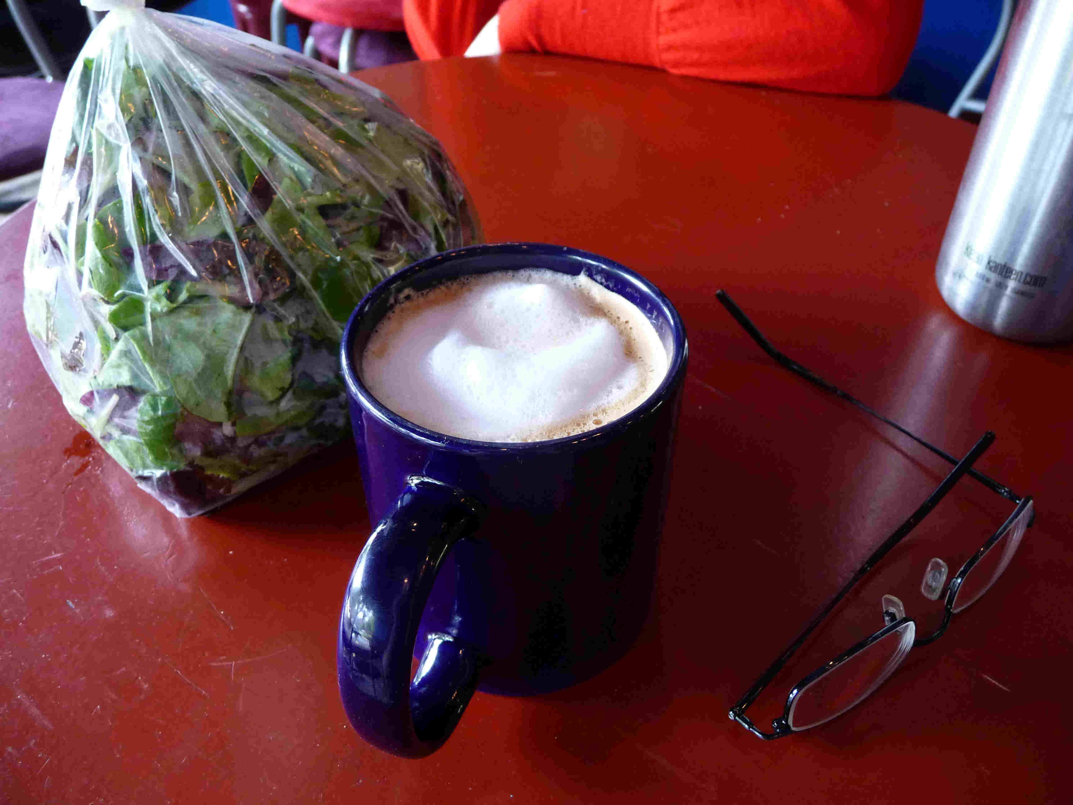 A cappuccino next to some mixed greens.